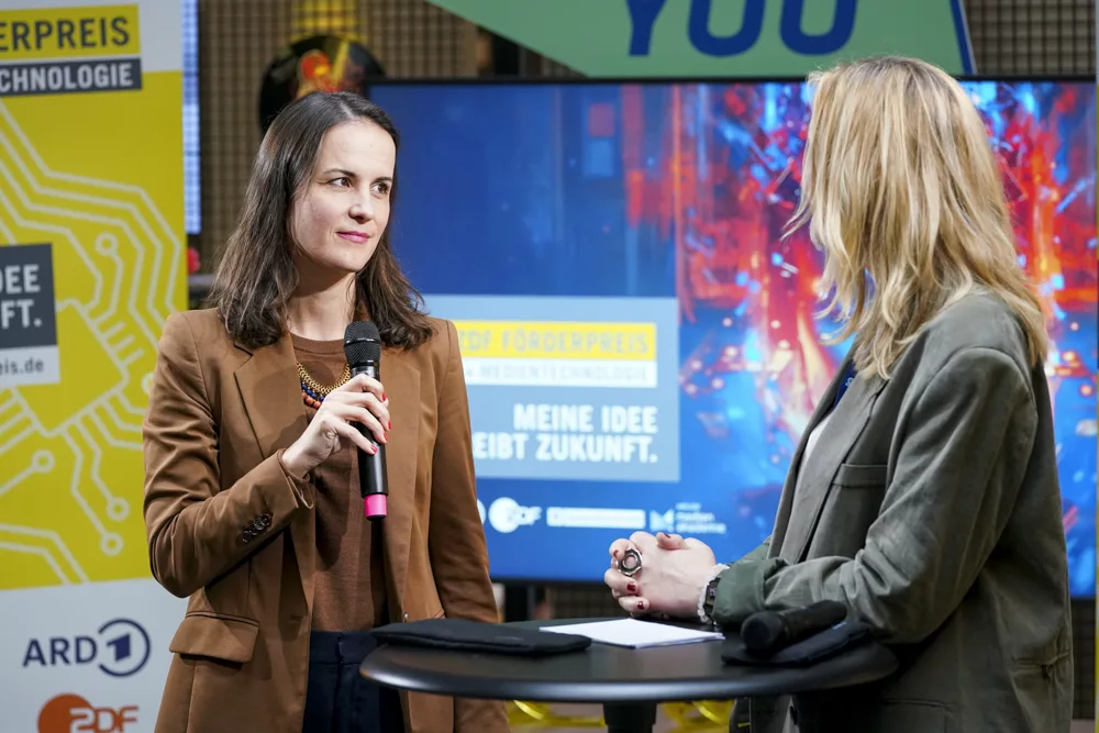 eventfotograf muenchen zwei Frauen sprechen am Mikrofon bei einer Preisverleihung im Hintergrund ein Bildschirm mit Grafiken