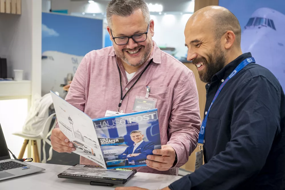 eventfotograf muenchen zwei maenner lachen und lesen gemeinsam eine zeitschrift am messestand