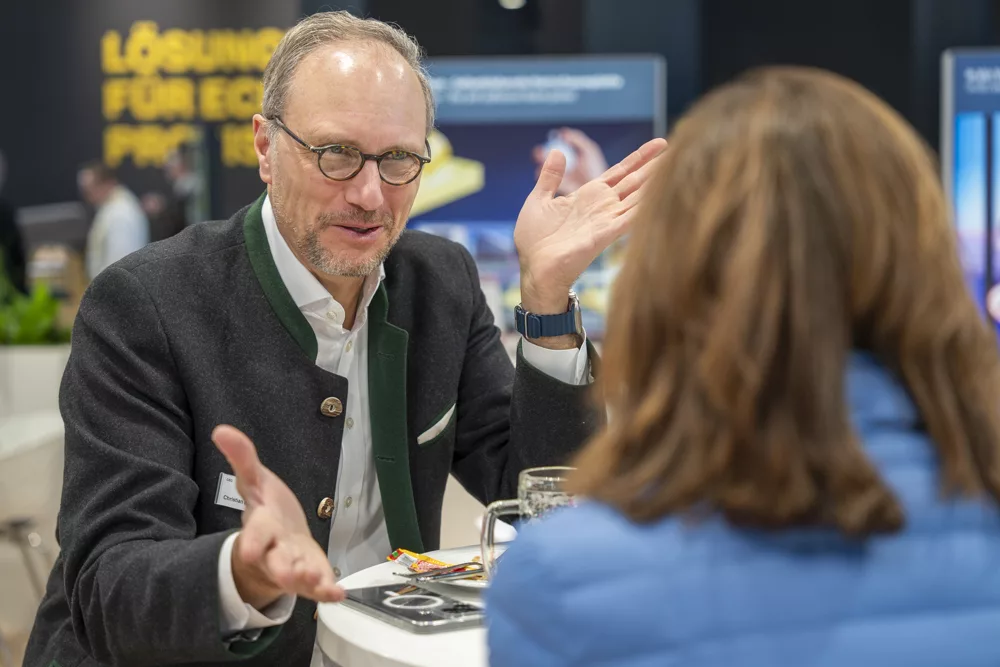 eventfotograf muenchen Gespraech zwischen zwei Personen am Tisch mit gestikulierendem Mann
