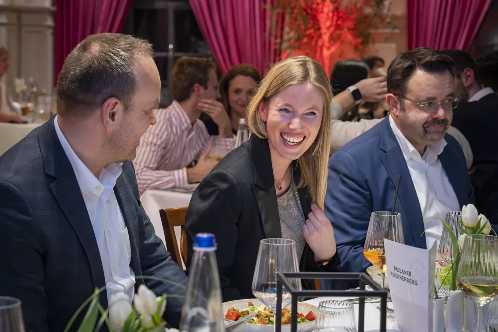 eventfotograf muenchen lachende Frau am Tisch bei festlichem Dinner mit gaesten